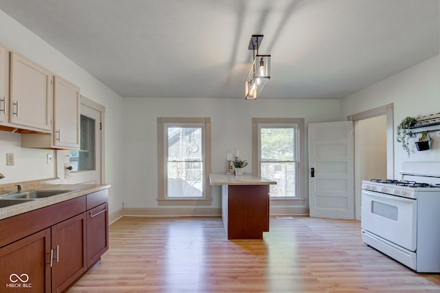 kitchen featuring light wood-type flooring, a sink, white gas range oven, light countertops, and baseboards