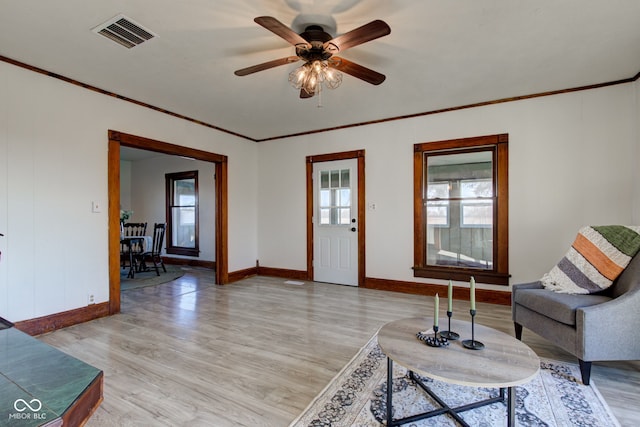 living room with baseboards, visible vents, light wood finished floors, and ornamental molding