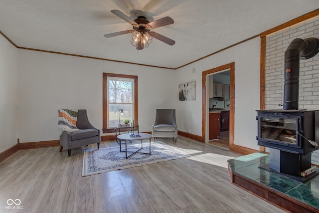 sitting room featuring a wood stove, wood finished floors, baseboards, and ornamental molding