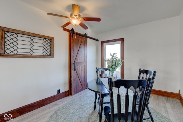 dining area featuring light wood finished floors, baseboards, a barn door, and a ceiling fan