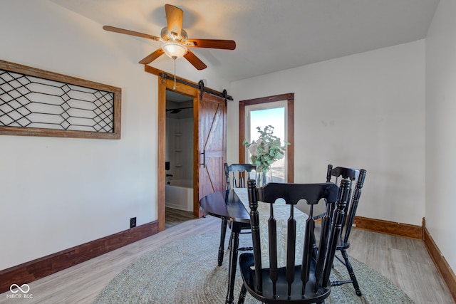 dining space with a barn door, light wood-style floors, baseboards, and ceiling fan