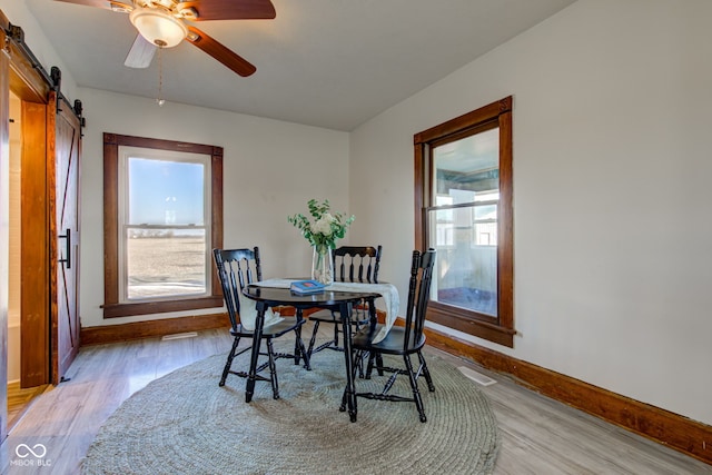 dining space with light wood-type flooring, a barn door, and a healthy amount of sunlight