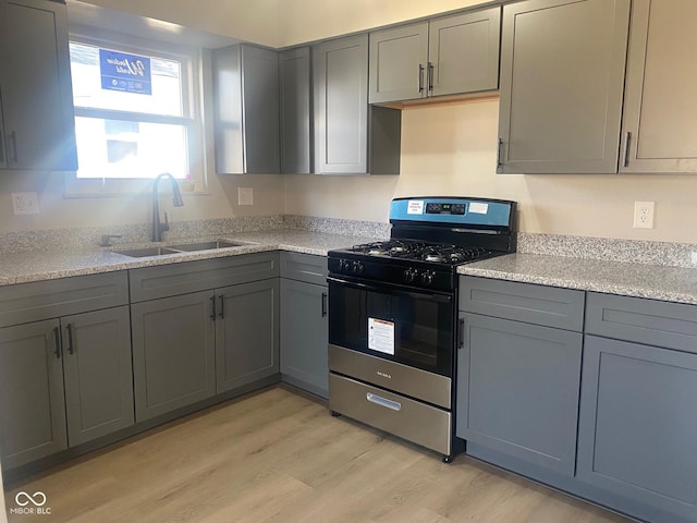 kitchen featuring a sink, light wood-style floors, gray cabinets, and stainless steel gas range oven