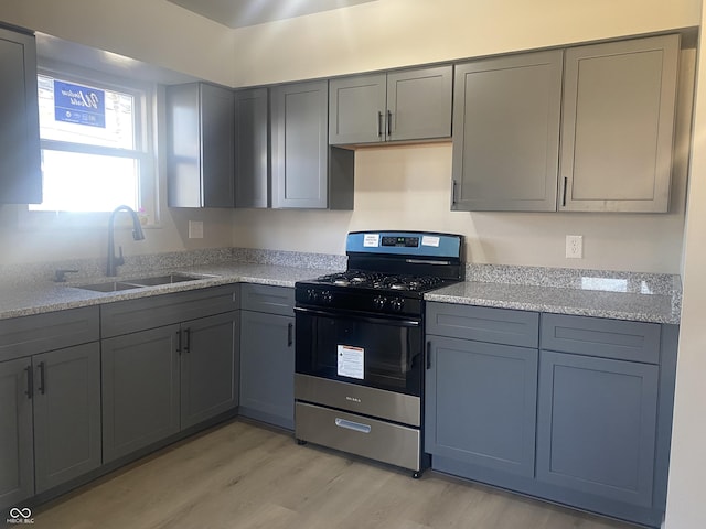 kitchen with gas range, gray cabinets, light wood finished floors, and a sink