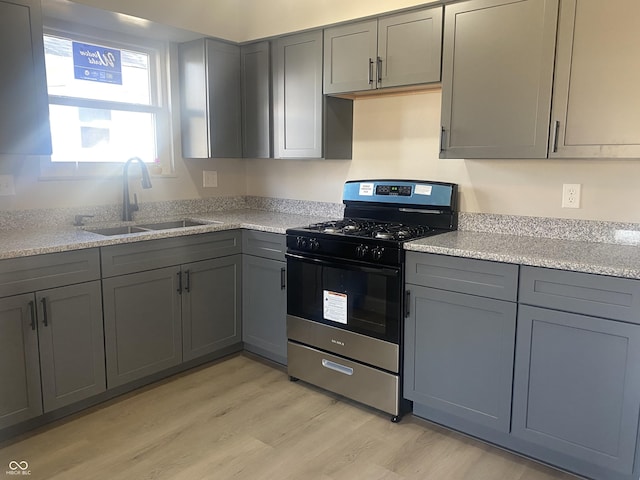 kitchen featuring gas range, light wood-style flooring, gray cabinets, and a sink