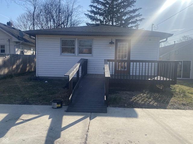 view of front of property with a shingled roof, a deck, and fence