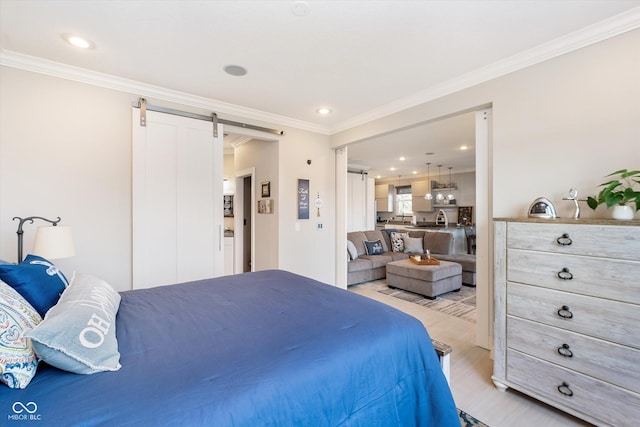 bedroom with a barn door, light wood-style floors, and ornamental molding