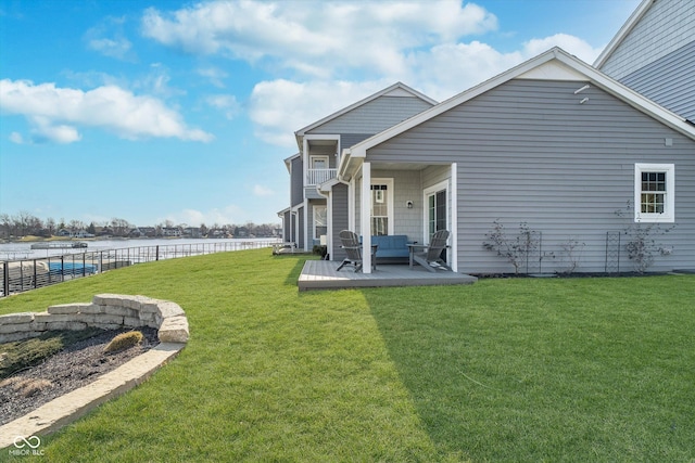 rear view of house with a balcony, a yard, fence, and a water view