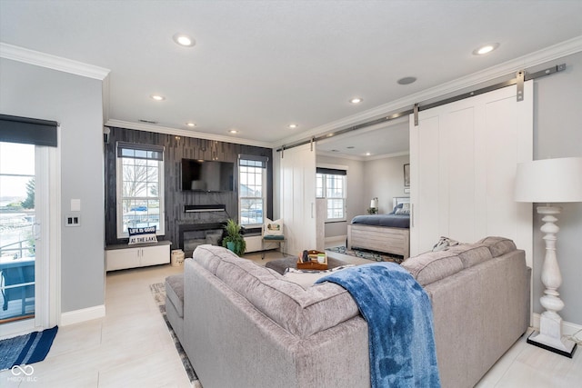 living area with baseboards, a barn door, ornamental molding, recessed lighting, and a glass covered fireplace