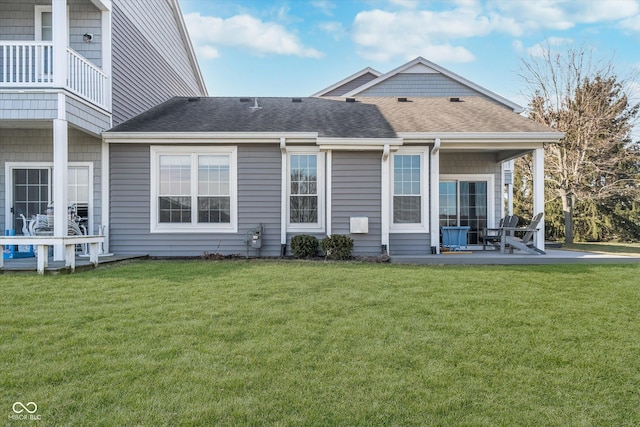 rear view of house featuring a yard, a patio, and roof with shingles