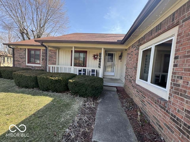 doorway to property featuring a porch, a yard, and brick siding