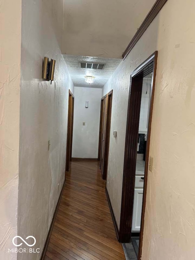 corridor with visible vents, a textured wall, and wood-type flooring