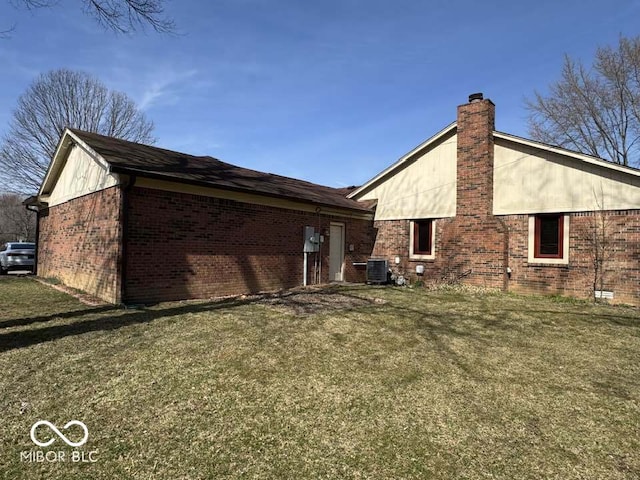 rear view of house featuring central air condition unit, a yard, brick siding, and a chimney