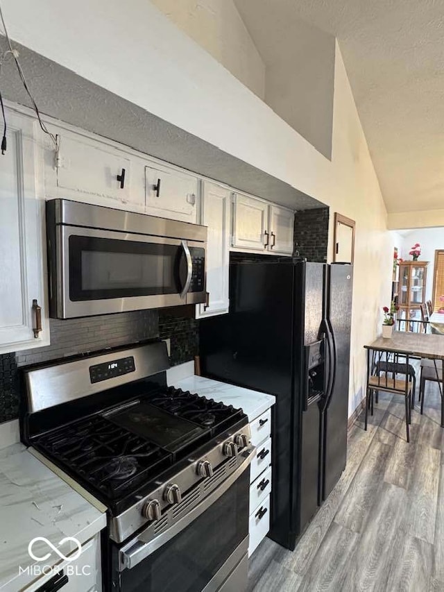 kitchen featuring vaulted ceiling, white cabinets, light countertops, appliances with stainless steel finishes, and tasteful backsplash