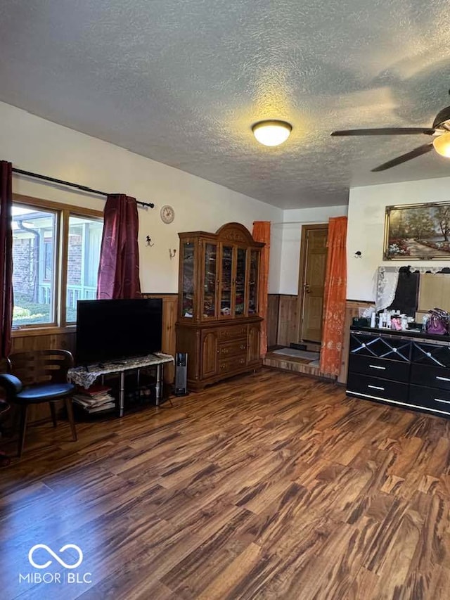 living room with ceiling fan, a wainscoted wall, a textured ceiling, and wood finished floors