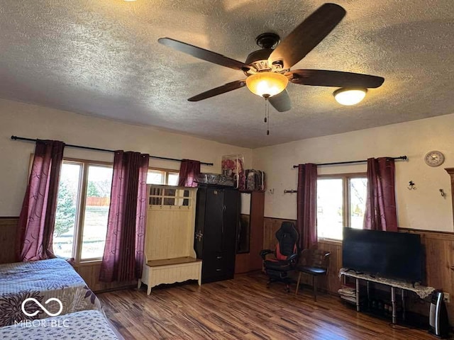 bedroom featuring a textured ceiling, wood finished floors, wood walls, wainscoting, and ceiling fan