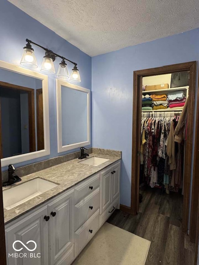 full bathroom with double vanity, wood finished floors, a walk in closet, and a sink