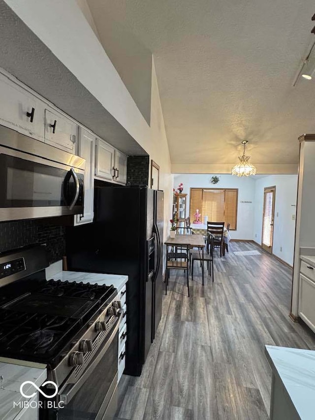 kitchen with wood finished floors, vaulted ceiling, appliances with stainless steel finishes, a textured ceiling, and white cabinetry