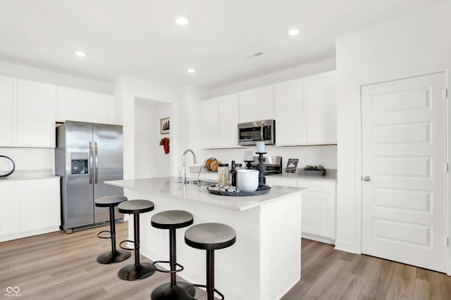 kitchen featuring an island with sink, a sink, a kitchen breakfast bar, stainless steel appliances, and light wood-style floors