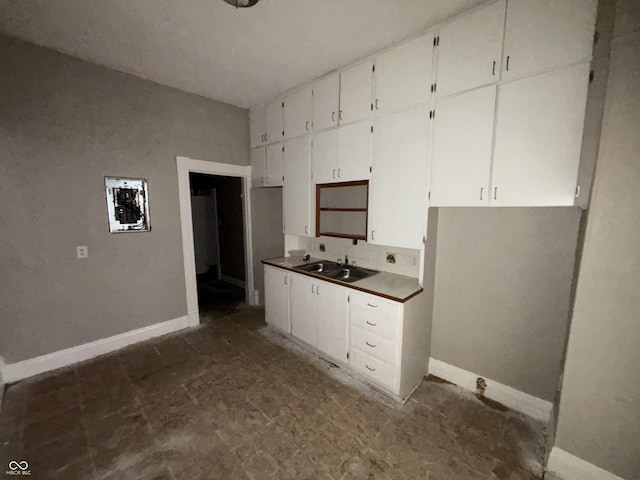 kitchen featuring white cabinets, baseboards, and a sink