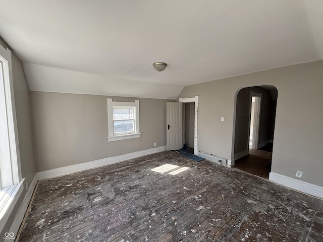 spare room featuring arched walkways, baseboards, and lofted ceiling