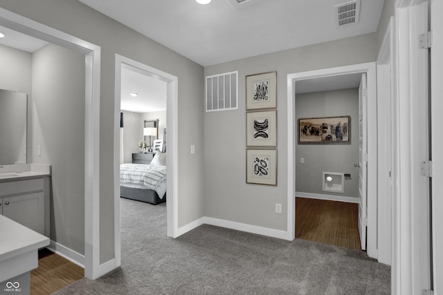 hall with dark colored carpet, visible vents, and baseboards