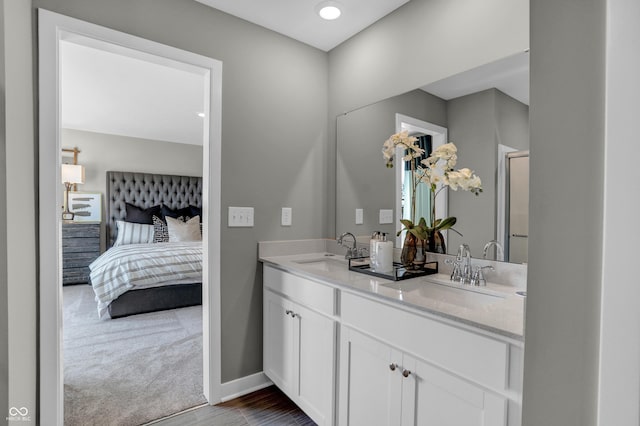 bathroom with double vanity, ensuite bathroom, baseboards, and a sink