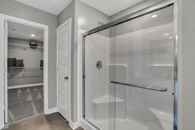 full bath with a walk in closet, a shower stall, baseboards, and wood finish floors