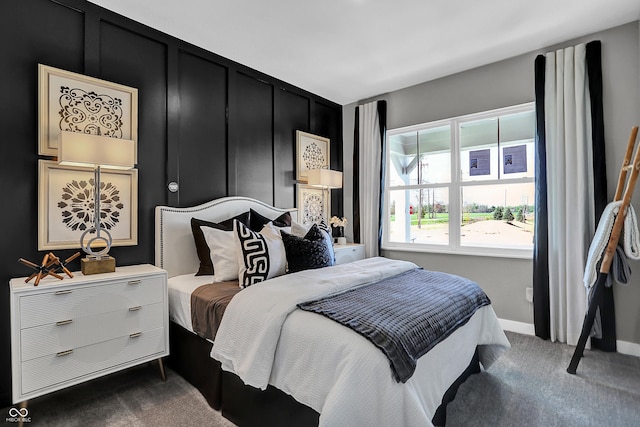 bedroom featuring a decorative wall, baseboards, and dark carpet