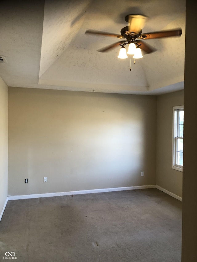 carpeted spare room with a tray ceiling, baseboards, and ceiling fan