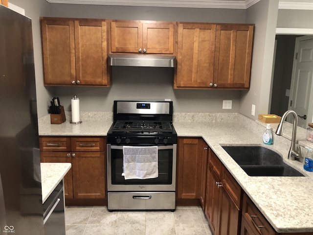 kitchen featuring under cabinet range hood, ornamental molding, freestanding refrigerator, stainless steel gas stove, and a sink