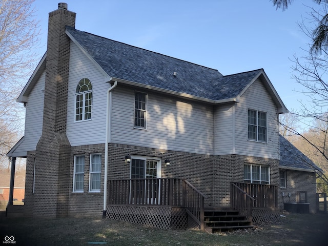 rear view of house with a wooden deck, brick siding, roof with shingles, and a chimney