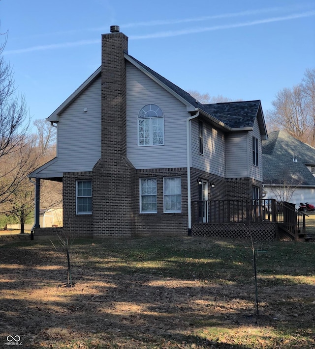 back of house featuring brick siding, a shingled roof, a wooden deck, a lawn, and a chimney