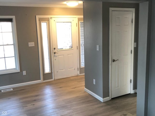 entryway featuring visible vents, baseboards, light wood-style floors, and ornamental molding