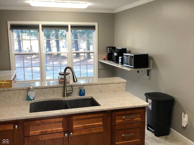 kitchen featuring light stone counters, stainless steel microwave, crown molding, and a sink