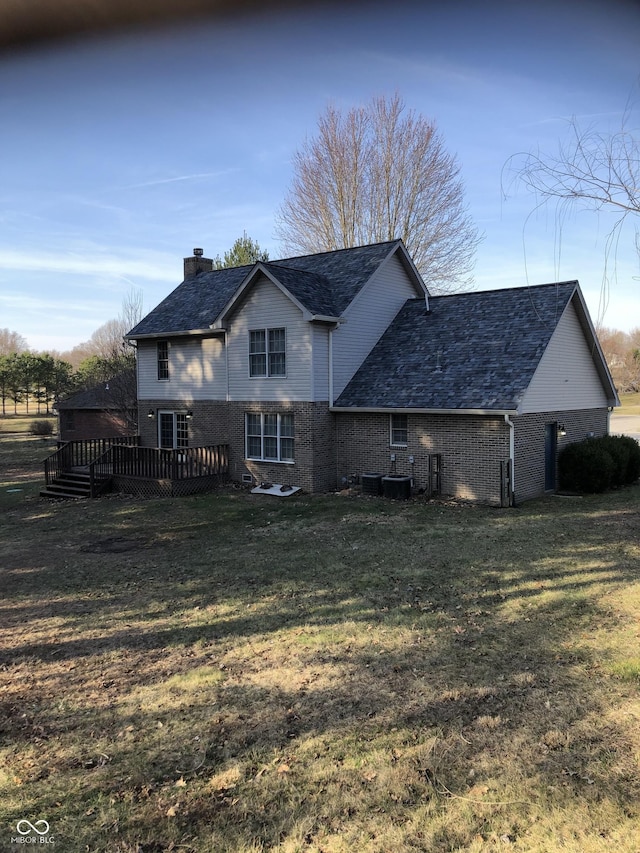 rear view of house featuring brick siding, roof with shingles, a chimney, a yard, and a deck