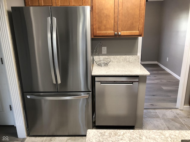 kitchen featuring brown cabinetry, stainless steel appliances, baseboards, and light stone countertops