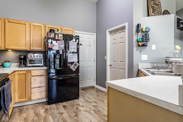 kitchen featuring light brown cabinetry, light wood-style flooring, a towering ceiling, black fridge with ice dispenser, and a sink