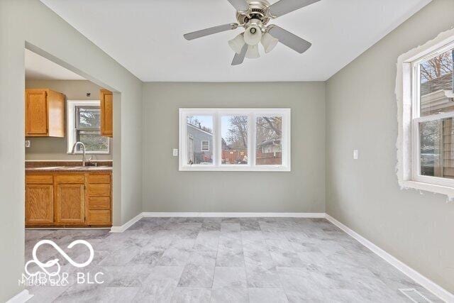 unfurnished dining area with a sink, baseboards, and ceiling fan