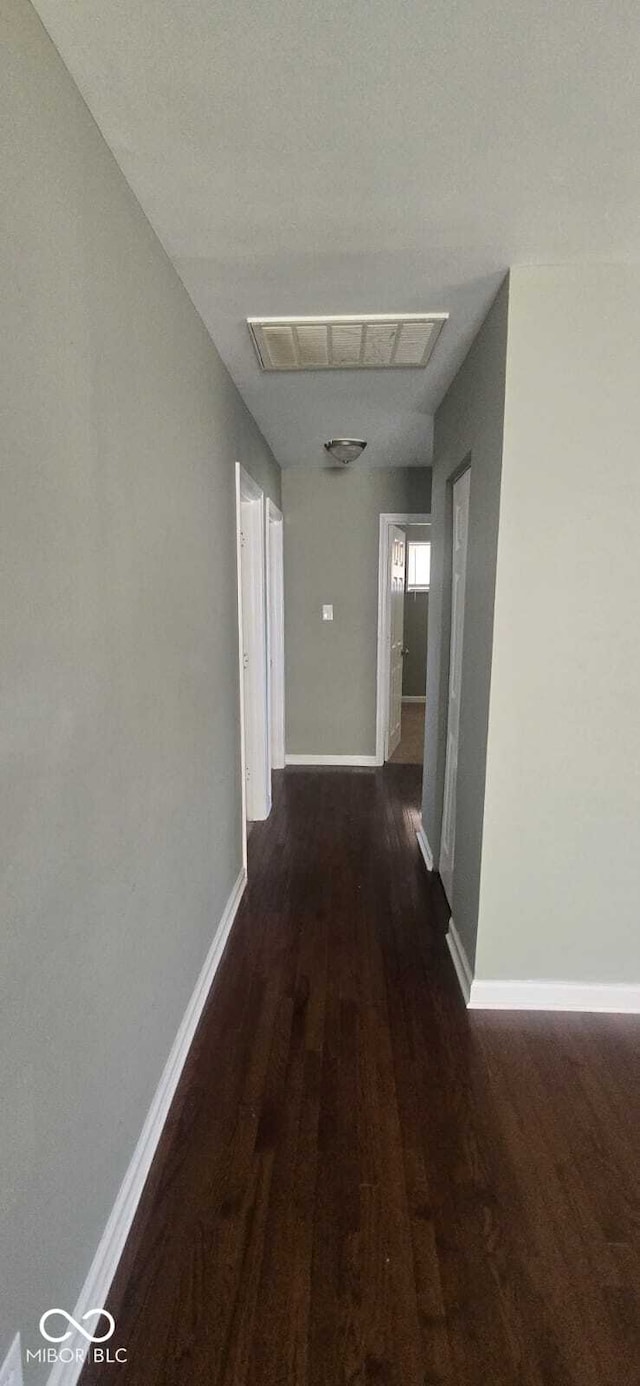 hallway with wood finished floors, baseboards, and visible vents