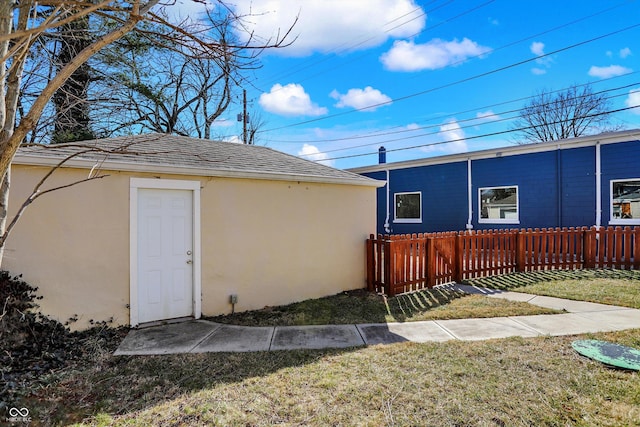 exterior space with an outbuilding, fence, a yard, a shingled roof, and stucco siding