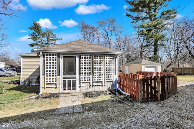 rear view of property with a garage, a shingled roof, an outdoor structure, and fence