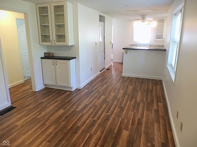 kitchen featuring dark countertops, glass insert cabinets, baseboards, and dark wood-style flooring