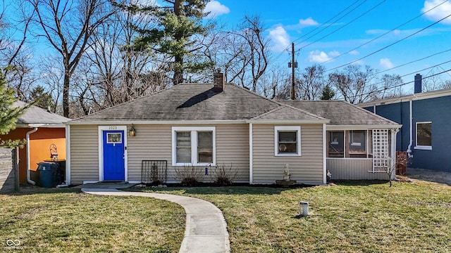 view of front of house with a front yard, a chimney, a sunroom, and a shingled roof