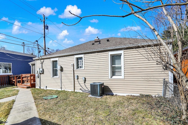 back of house with a yard, central AC unit, and a shingled roof