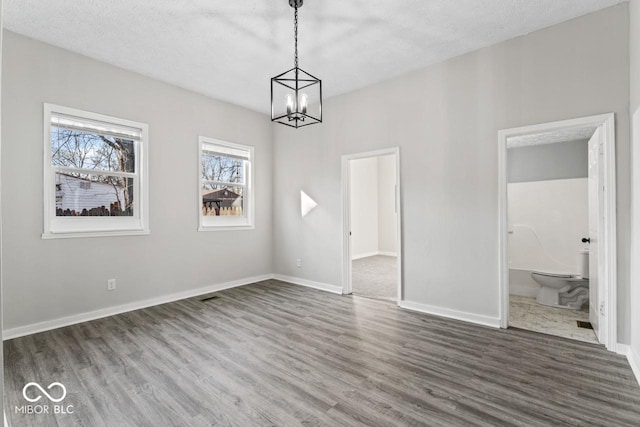 unfurnished dining area featuring baseboards, a textured ceiling, an inviting chandelier, and wood finished floors