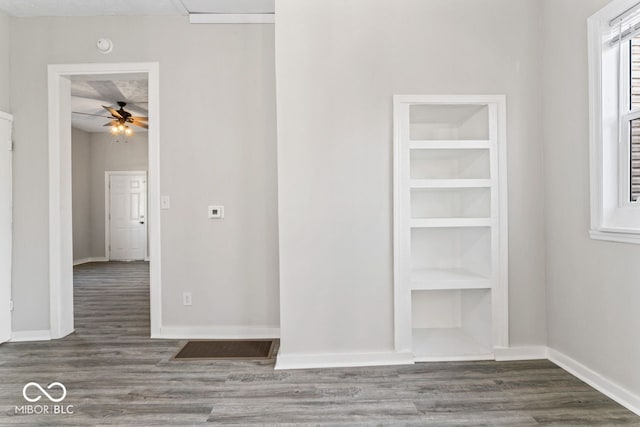 empty room featuring built in shelves, wood finished floors, baseboards, and ceiling fan