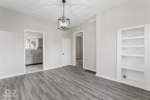 unfurnished dining area featuring baseboards, built in shelves, a textured ceiling, and wood finished floors