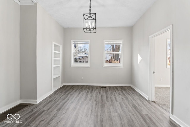 unfurnished dining area featuring an inviting chandelier, wood finished floors, and baseboards