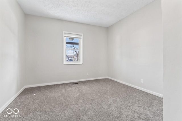 spare room with carpet flooring, visible vents, baseboards, and a textured ceiling